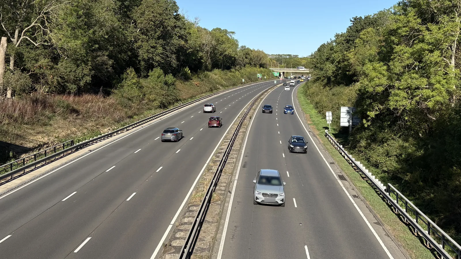 A dual carriageway seen from a footbridge, with traffic in both directions and trees on either side